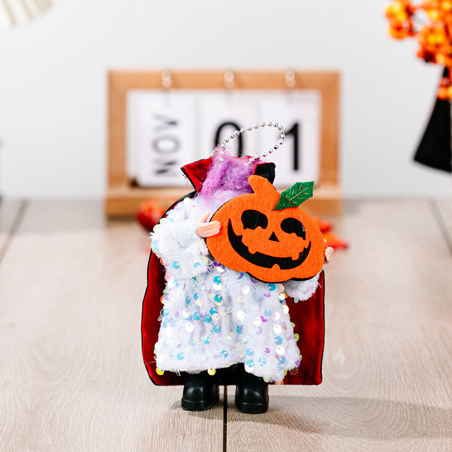 Halloween doll in sequin cape holding a pumpkin, with a black cape and white sequin dress.