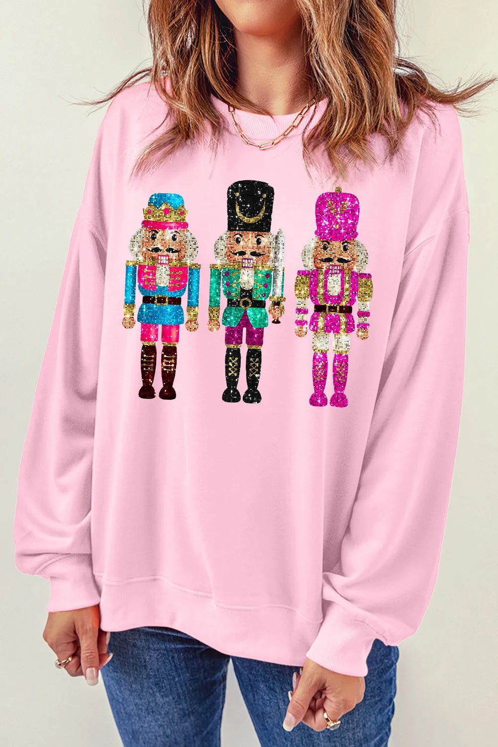 Blush pink crewneck sweatshirt with a graphic of three sequined nutcrackers.