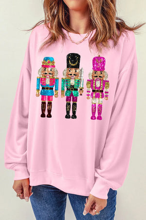 Blush pink crewneck sweatshirt with a graphic of three sequined nutcrackers.