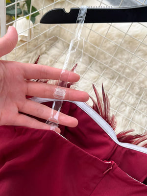 Wine red strapless jumpsuit with feather trim and clear adjustable straps.