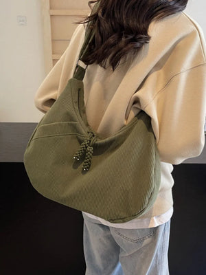 Moss green corduroy crescent shoulder bag with braided tassel detail and adjustable strap.