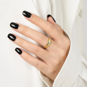 Gold grooved band ring with aquamarine eye detail on a hand with black nails