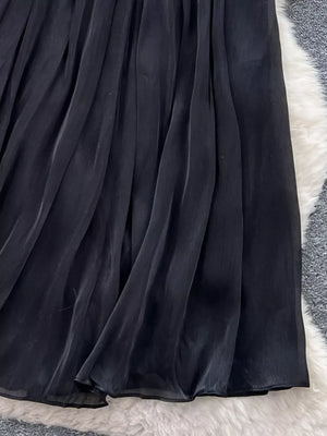 Black pleated maxi skirt with flowing fabric and a sheer hem detail.