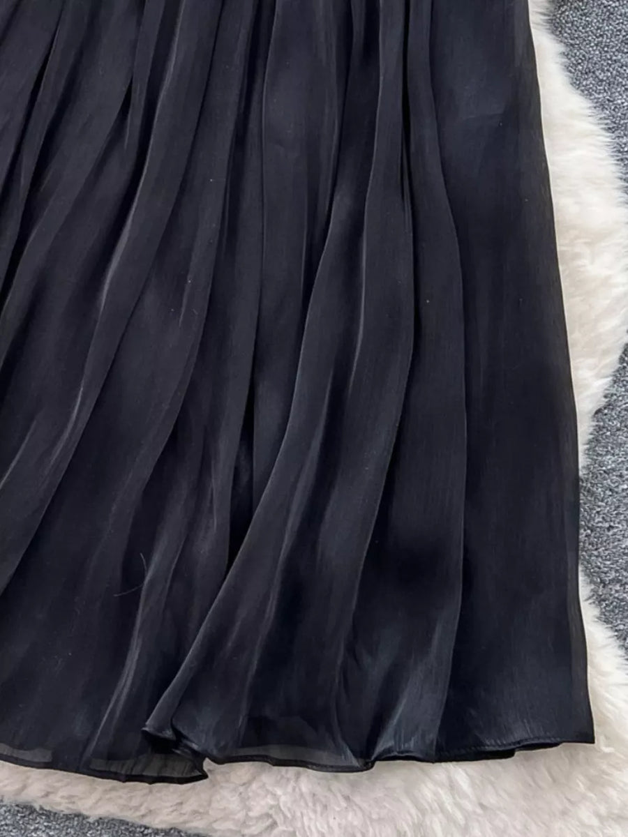 Black pleated maxi skirt with flowing fabric and a sheer hem detail.