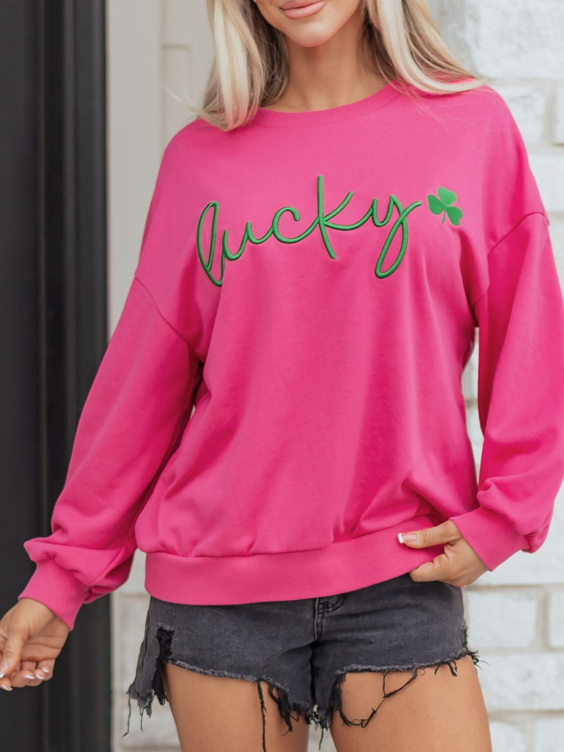 Pink crew neck sweatshirt with green embroidered lucky clover graphic and text