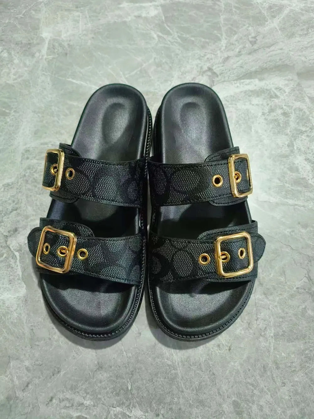 Black slide sandals with double buckle detail and all-over logo pattern.