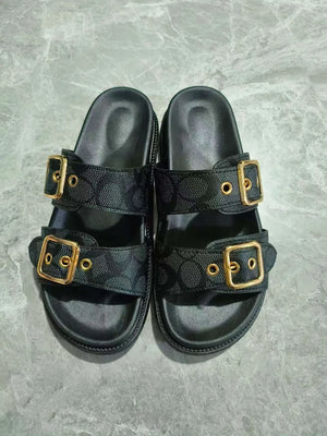 Black slide sandals with double buckle detail and all-over logo pattern.