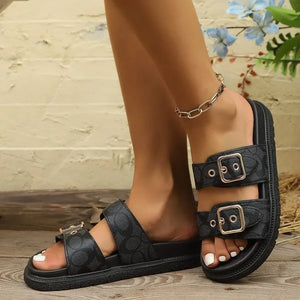 Black double strap logo slides with gold buckles and textured footbed.