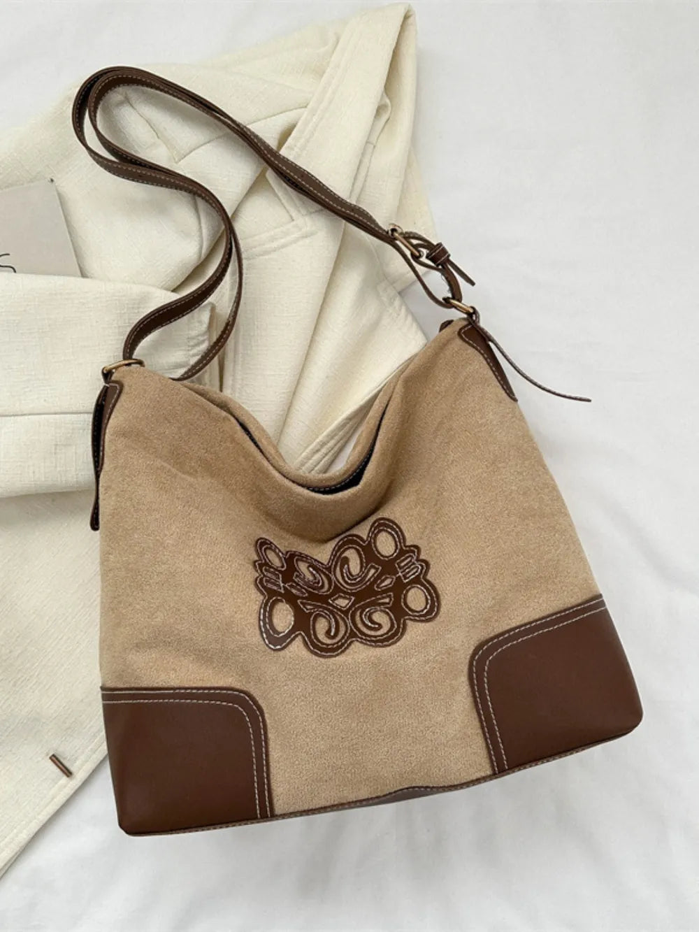 Khaki suede hobo bag with brown leather trim and contrast stitching, featuring a large appliqué detail.