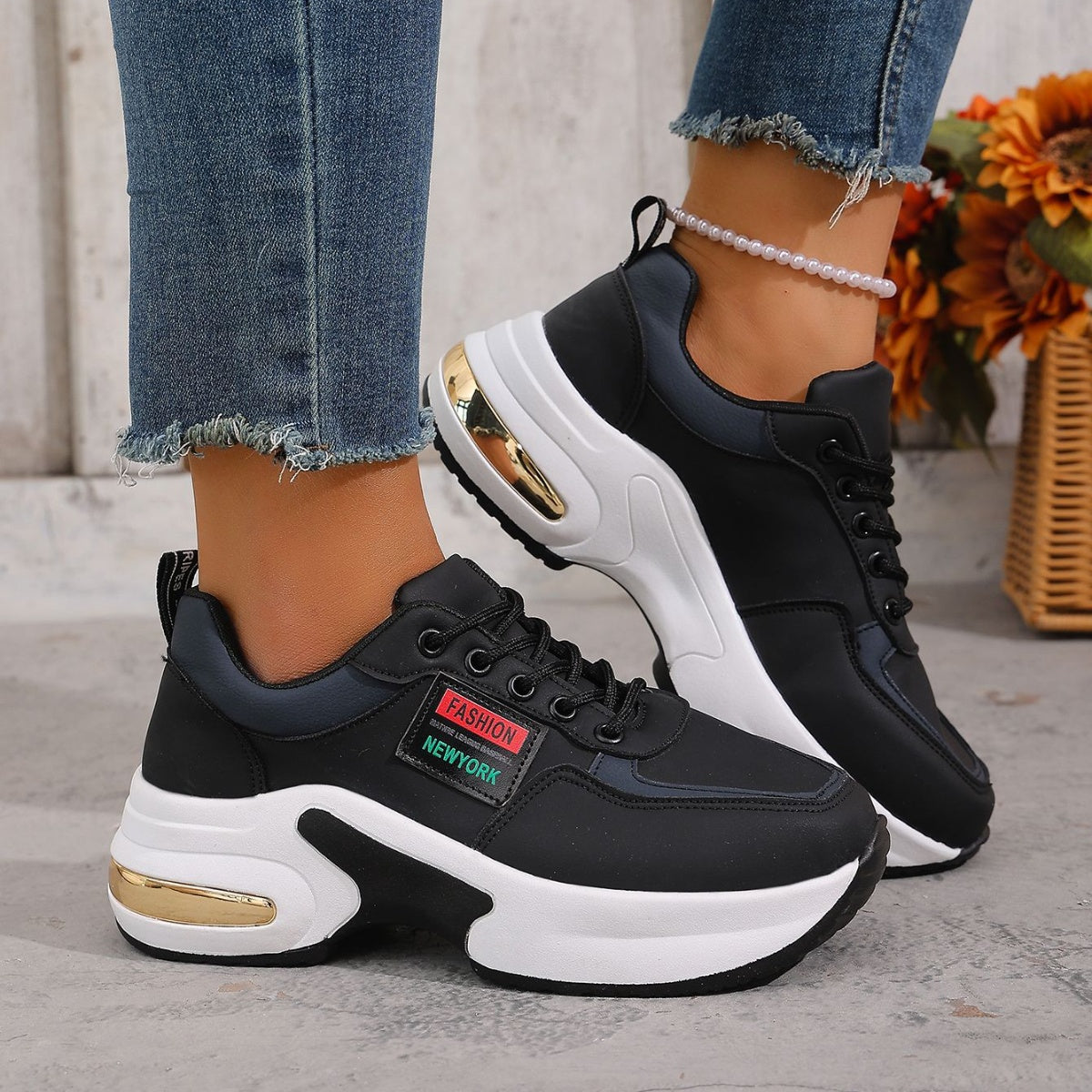 Black lace-up sneakers with white chunky sole and gold accents.