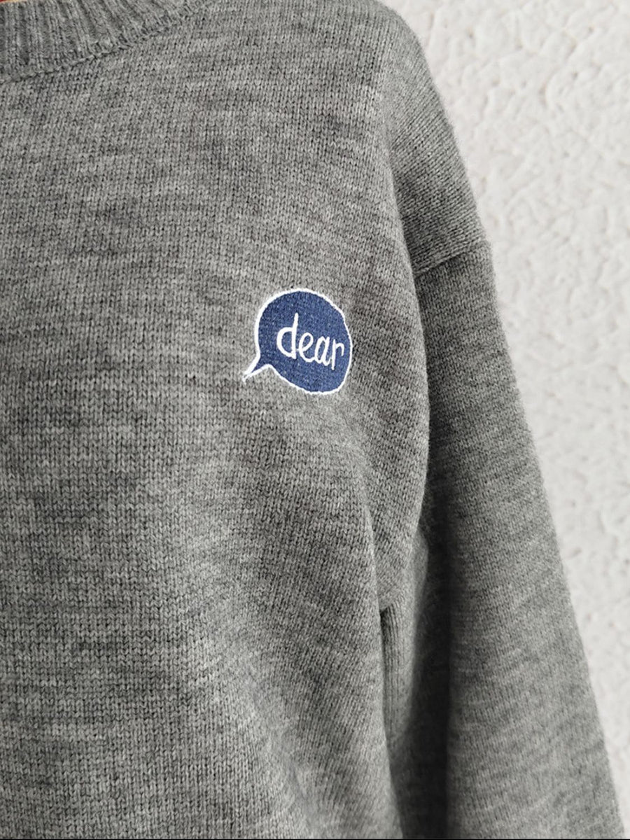Dark gray acrylic knit sweater with embroidered "dear" speech bubble detail on chest.