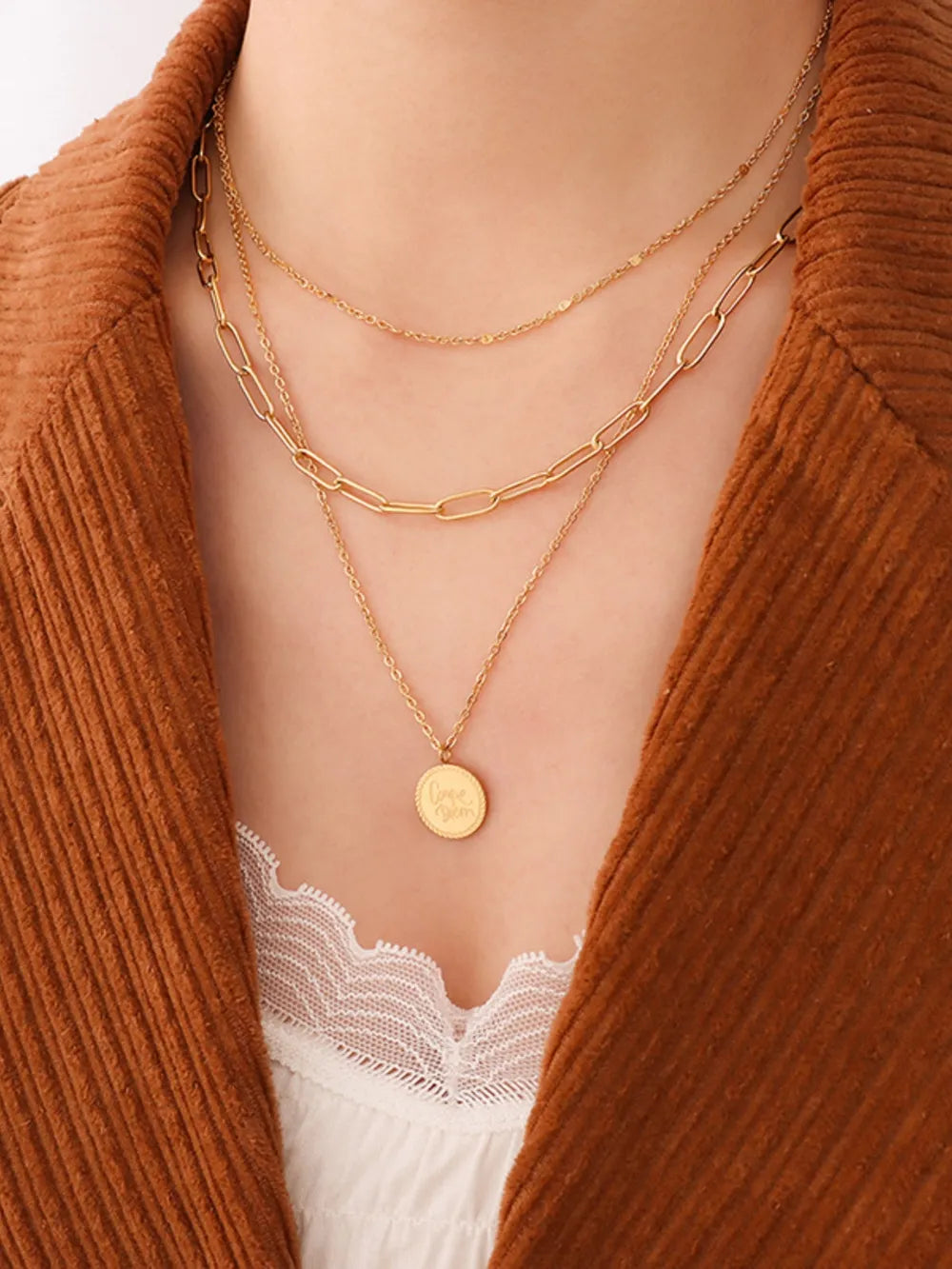Gold layered chain necklace with oval pendant, styled with a white lace camisole and brown jacket.