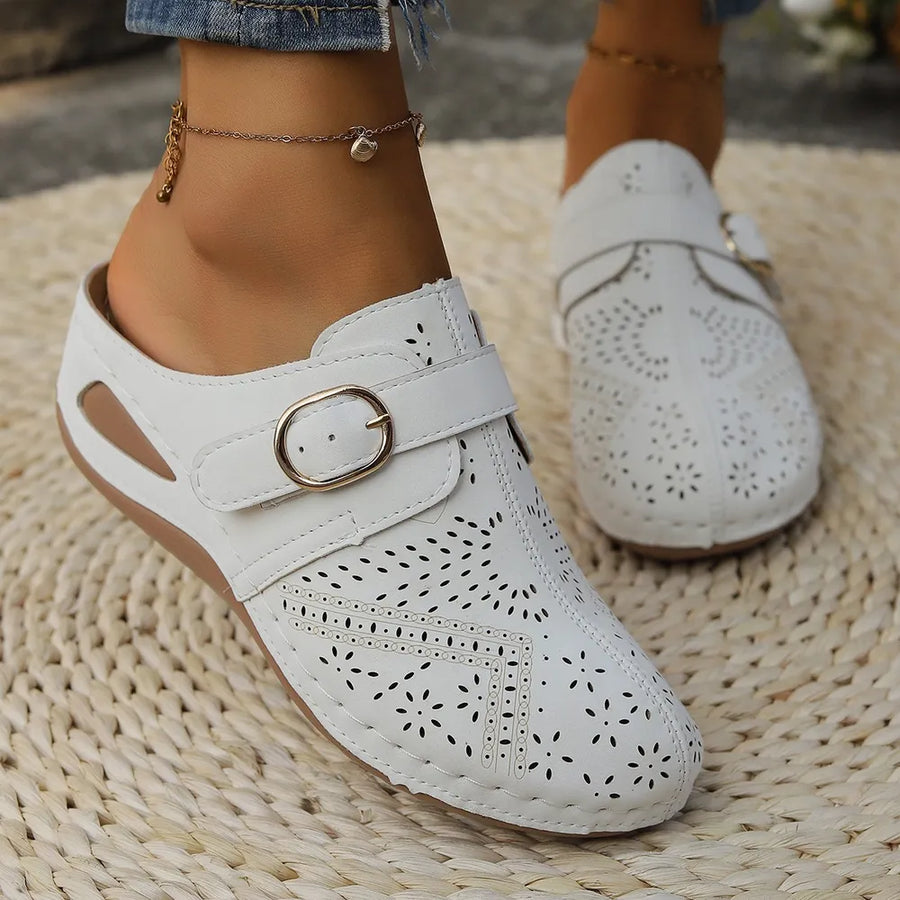 White laser-cut buckle mule wedges with perforated details and a gold buckle.