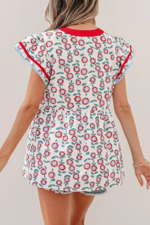 White cotton blouse with red and blue floral print, ruffle sleeves, and contrast trim.