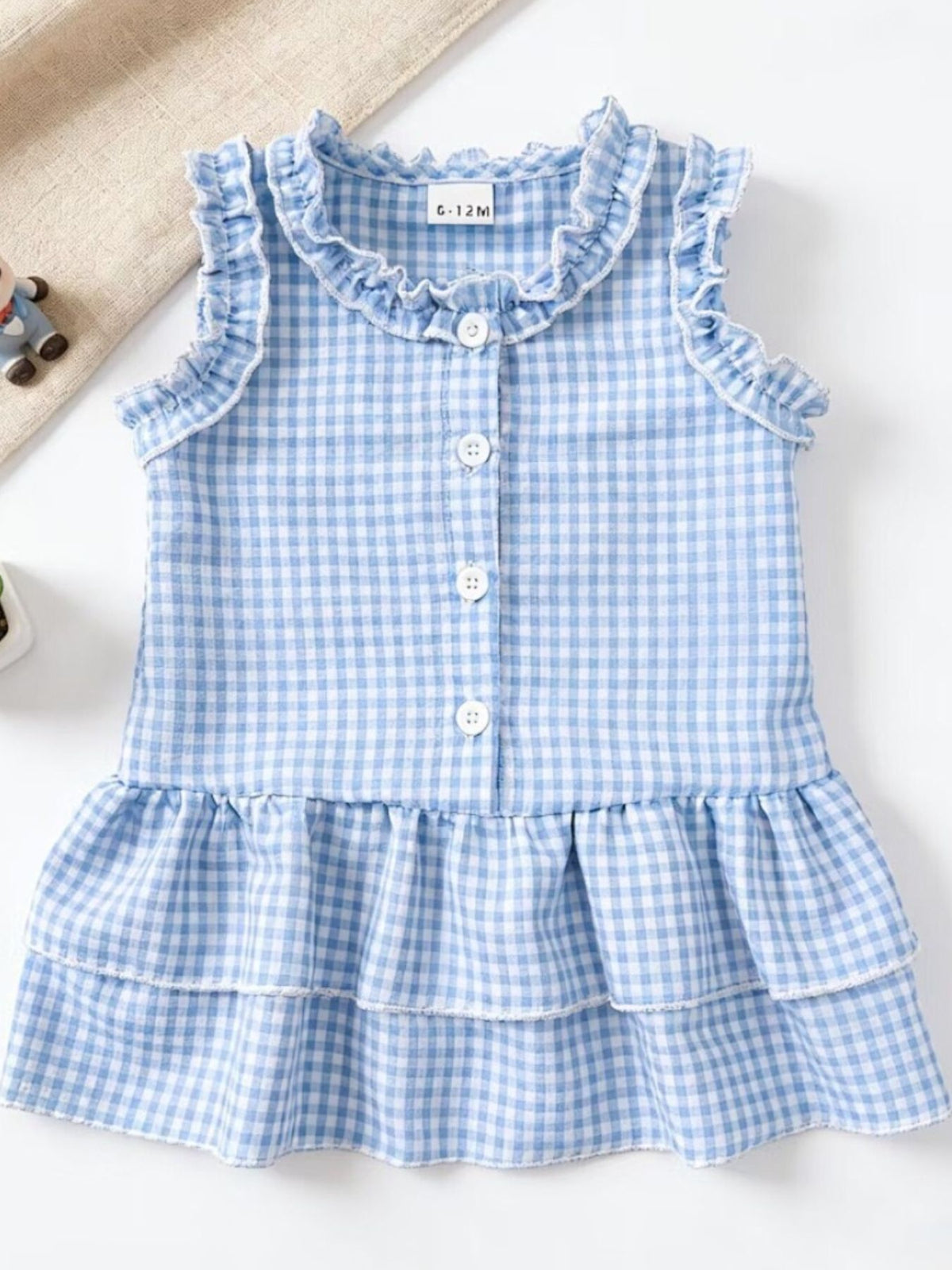 Baby dress in pastel blue gingham with ruffled neckline and tiered skirt.