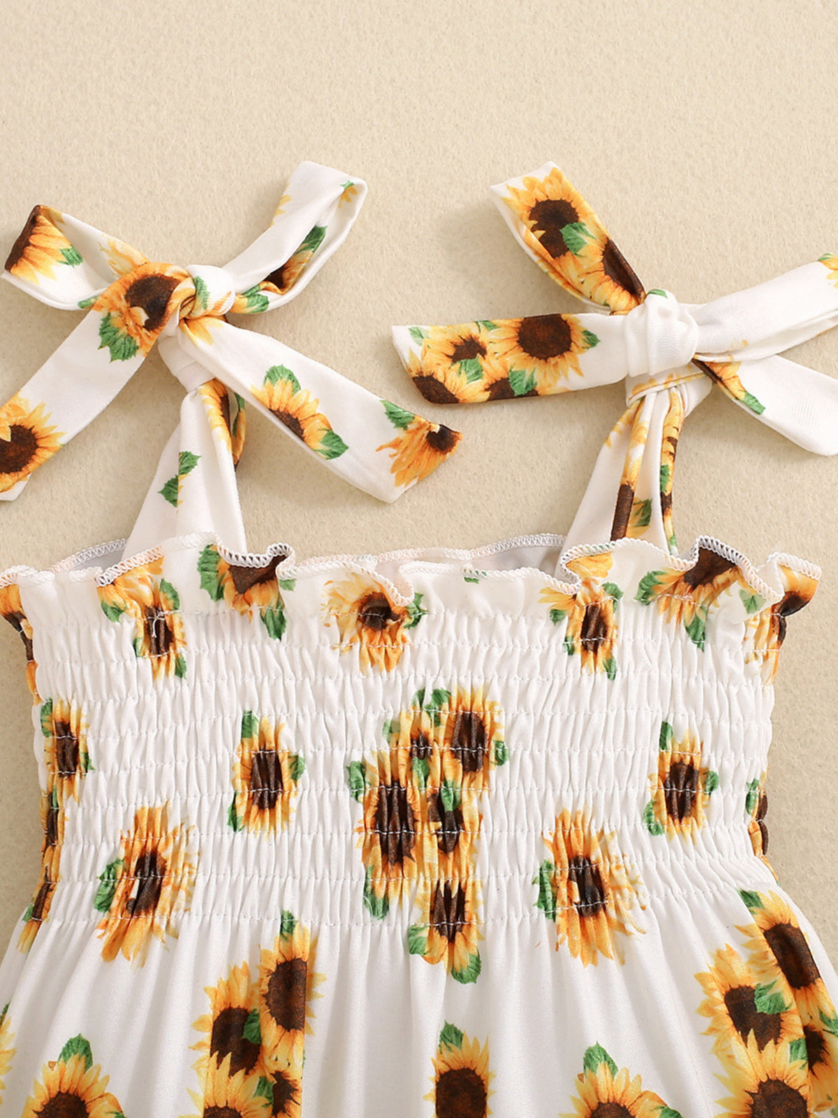 Baby jumpsuit with sunflower print, smocked bodice, and tie straps.