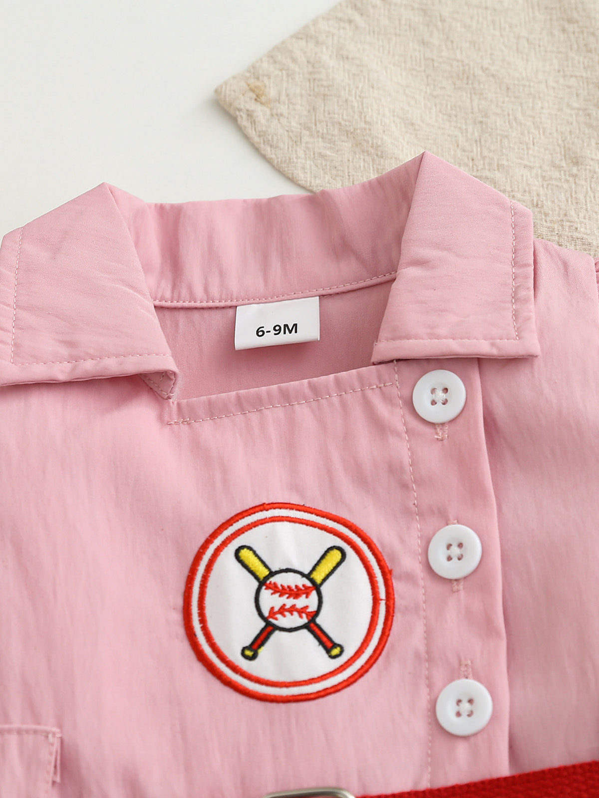 Pink cotton blend baseball dress for baby girls with embroidered baseball patch and white buttons.