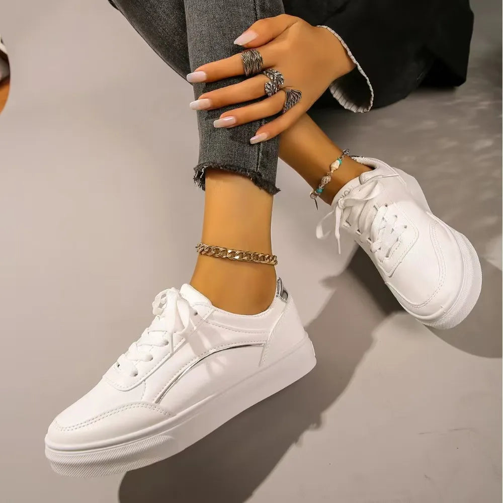 White sneakers with minimalist metallic trim detail and white laces.