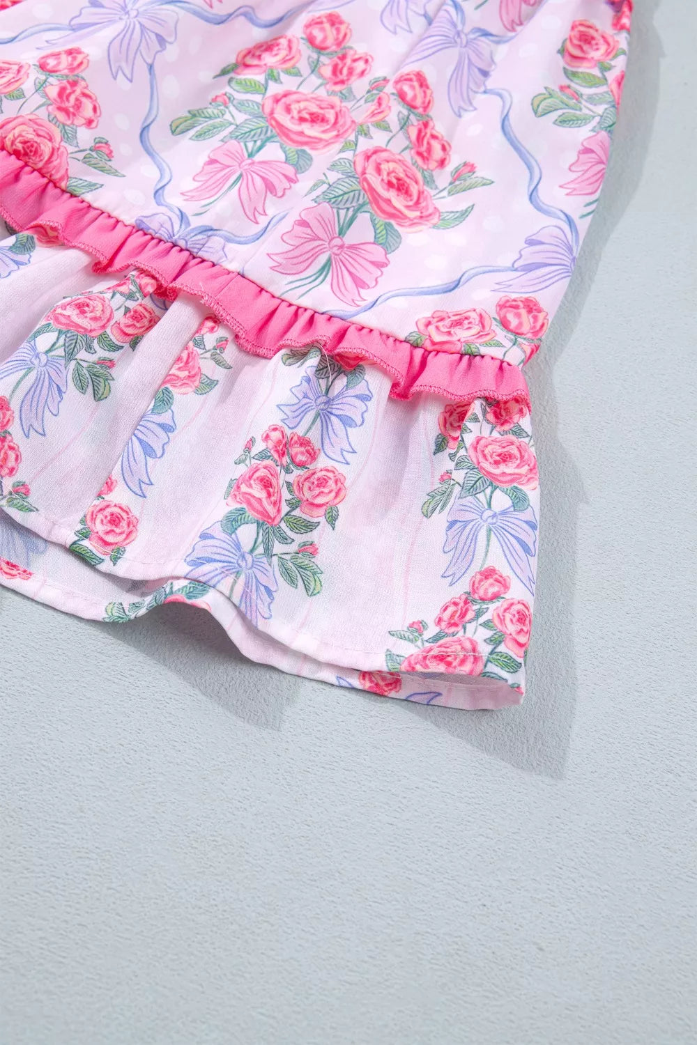 Floral tiered ruffle dress with pink roses and blue bows on a white background.