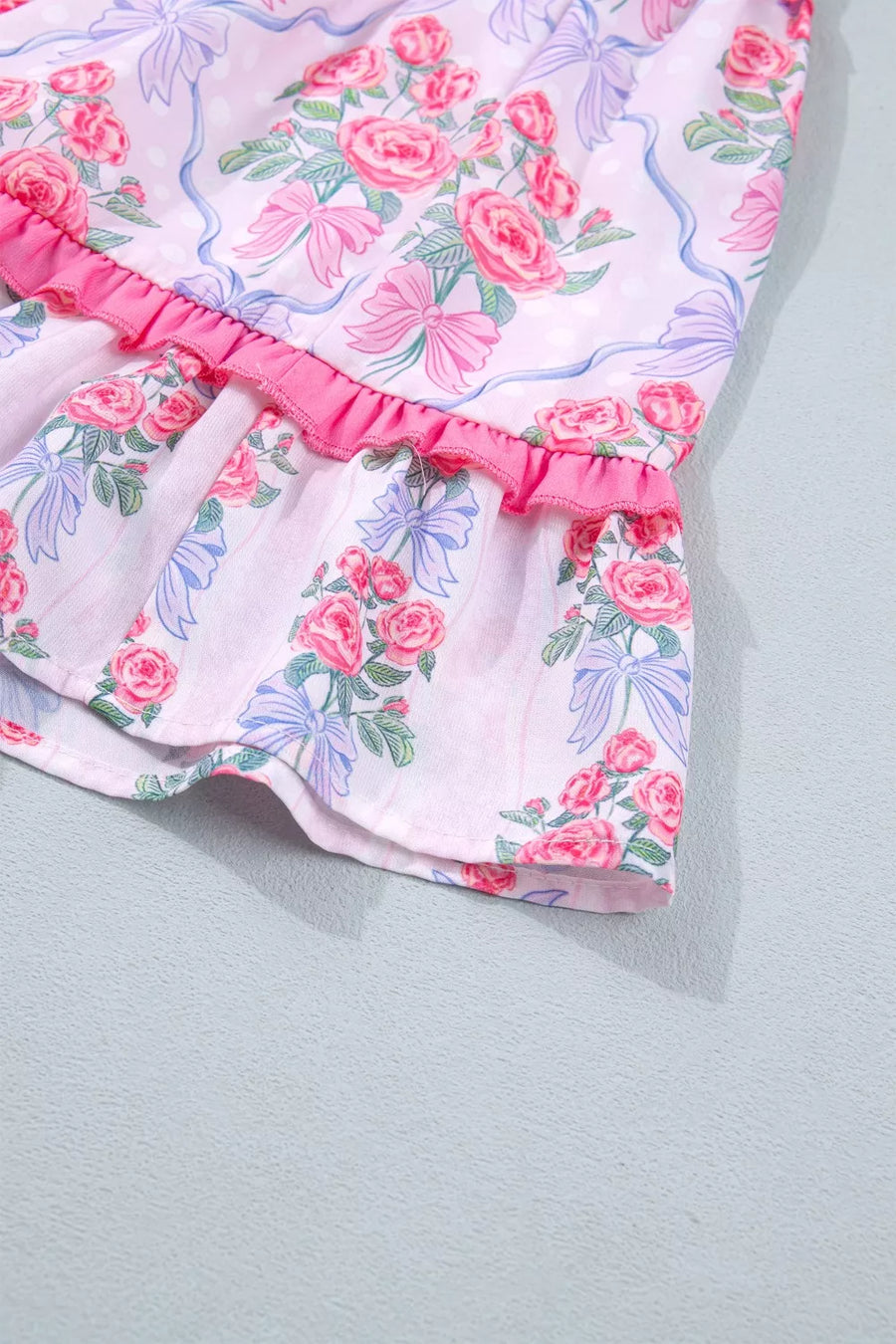 Floral tiered ruffle dress with pink roses and blue bows on a white background.