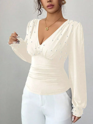Beige ruched V-neck blouse with pearl embellishments and long sleeves.