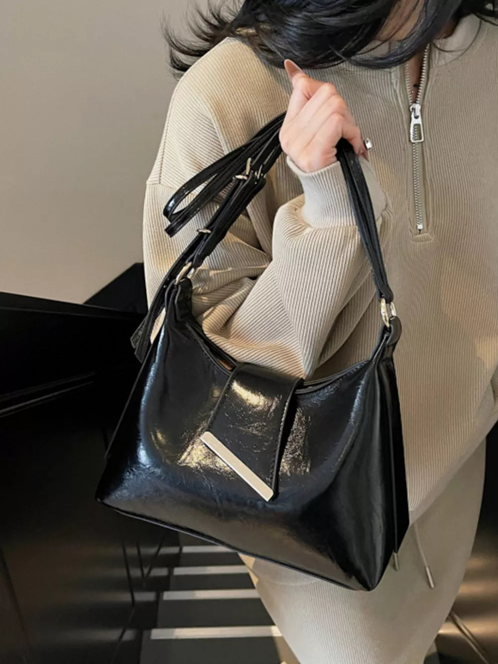Black patent crossbody bag with adjustable strap and silver hardware detail.