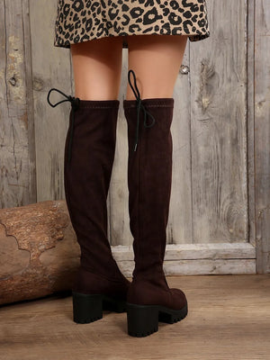 Brown over-the-knee boots with back lacing and lug sole.