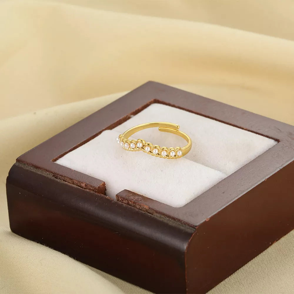 Gold adjustable ring with pearl embellishments on a white cushion in a wooden box.