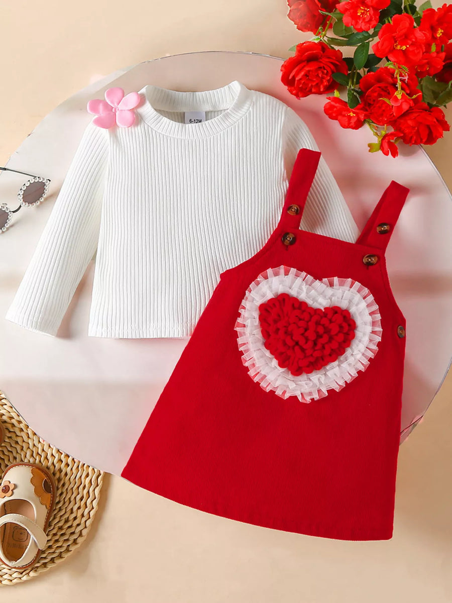 Red corduroy pinafore dress with heart detail and white ribbed long sleeve shirt.