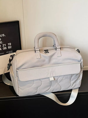 Luxurious quilted duffel bag in light gray with adjustable strap and top handles.