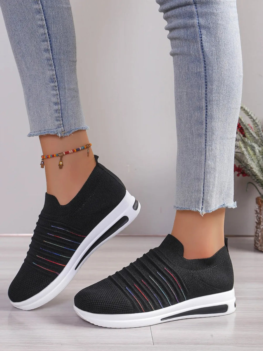 Black knit slip-on wedge sneakers with rainbow stripe detail and white soles.