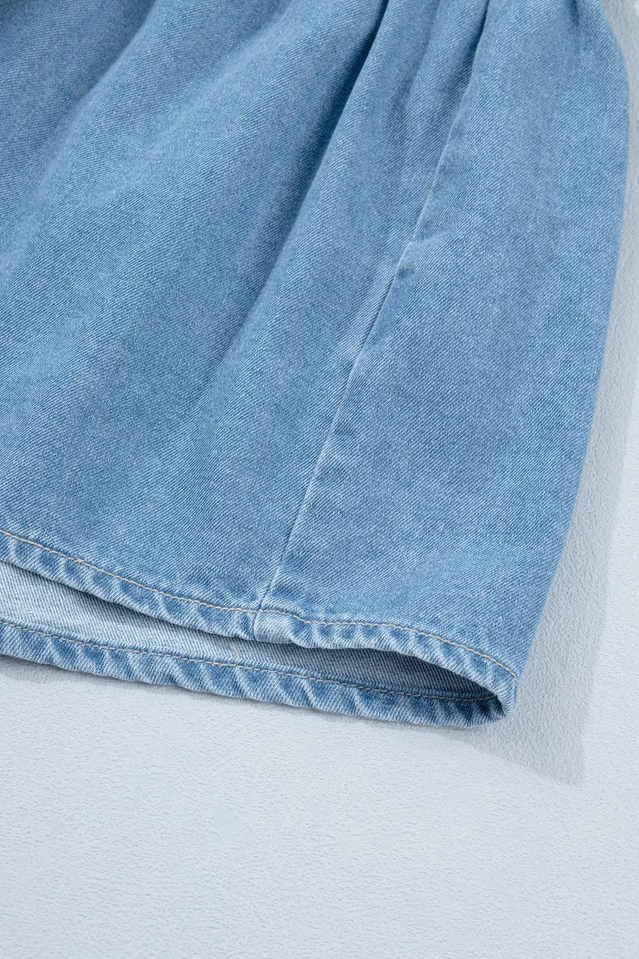 Light blue denim dress detail showing ruffled hem and stitching.