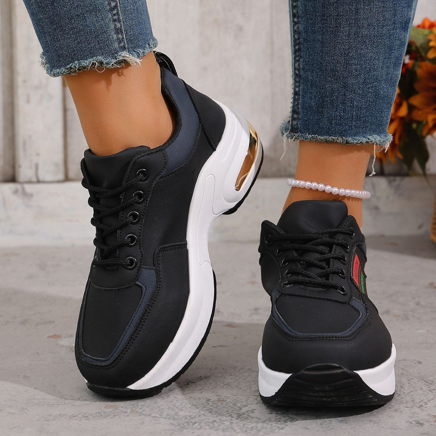 Black lace-up sneakers with a chunky white sole and gold heel detail.