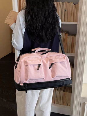 Pink duffel bag with black accents and two front pockets, worn by a person holding a book.