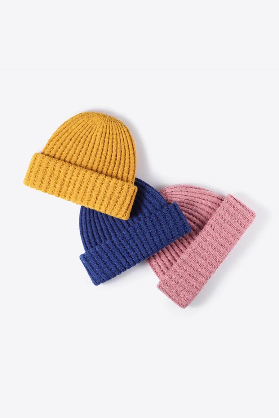 Textured ribbed knit beanies in mustard, indigo, and pink acrylic.