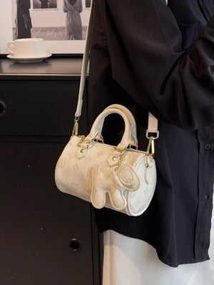 White mini barrel crossbody bag with embossed pattern and charm detail