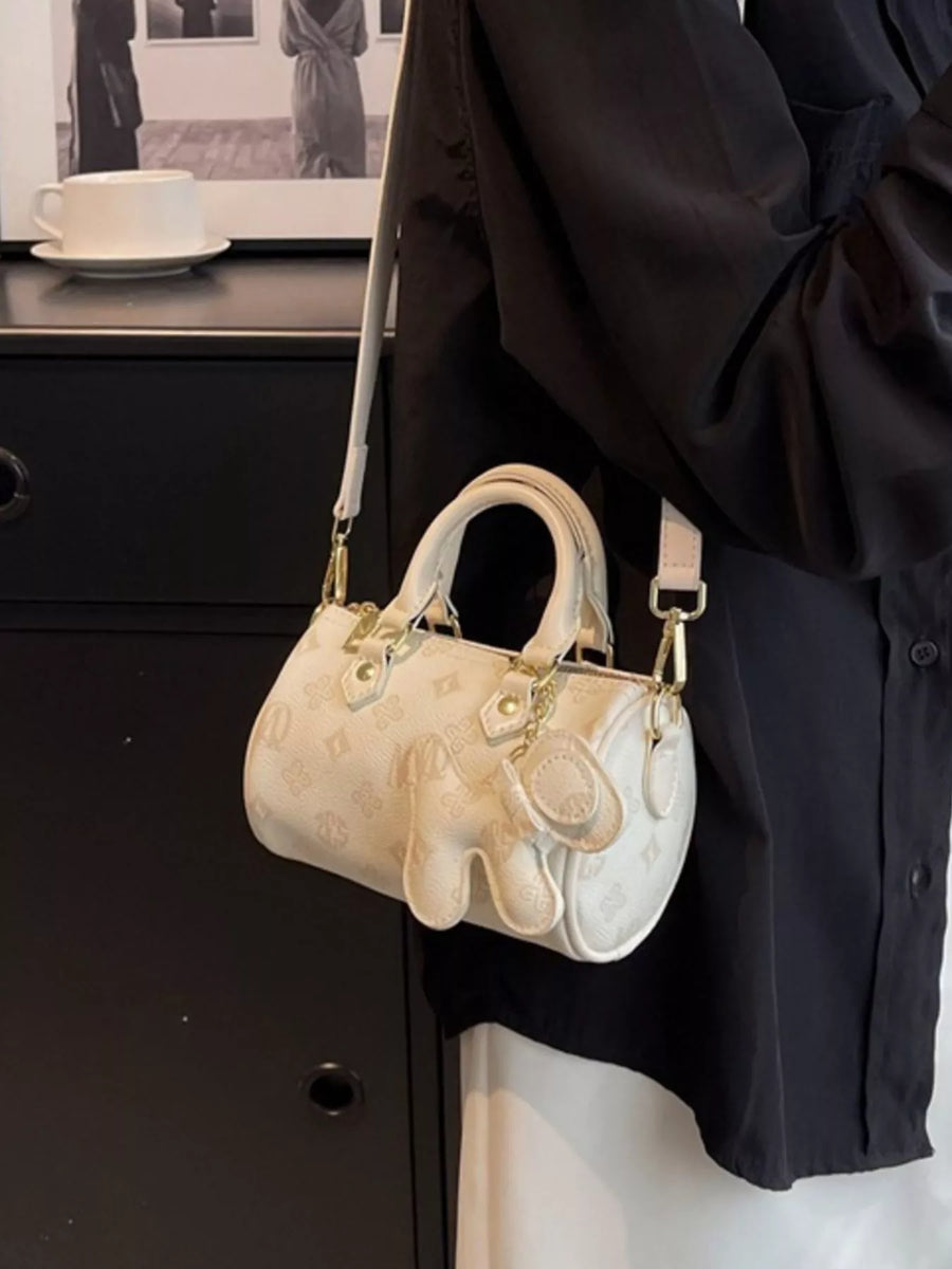 White mini barrel crossbody bag with embossed pattern and charm detail