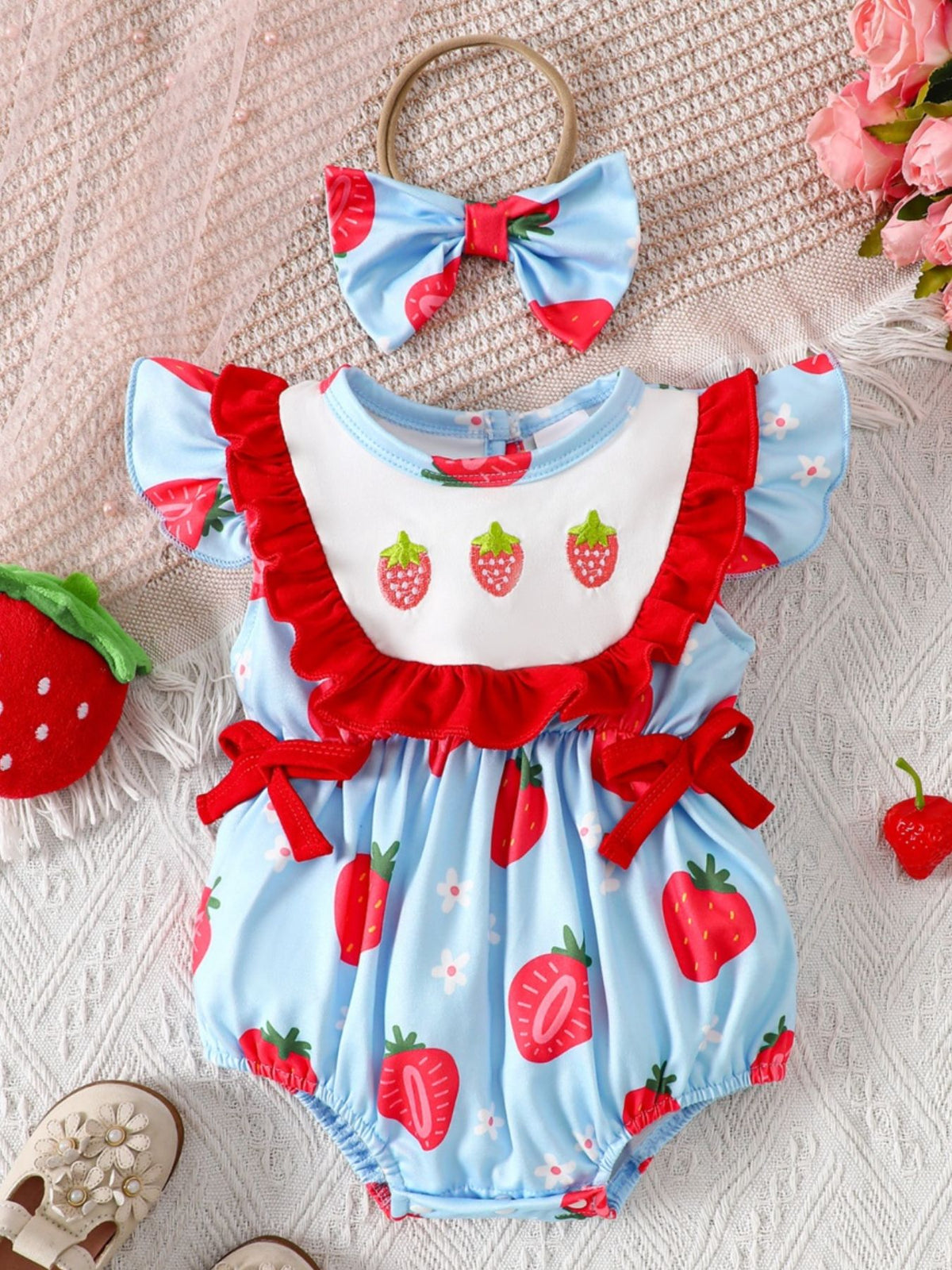 Baby one-piece set in pastel blue with strawberry floral print, ruffle trim, and bow details.