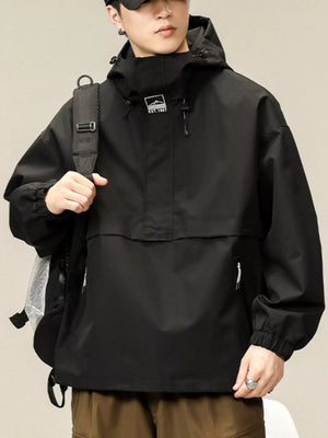 Black oversized hooded windbreaker jacket with chest logo and zippered pockets.