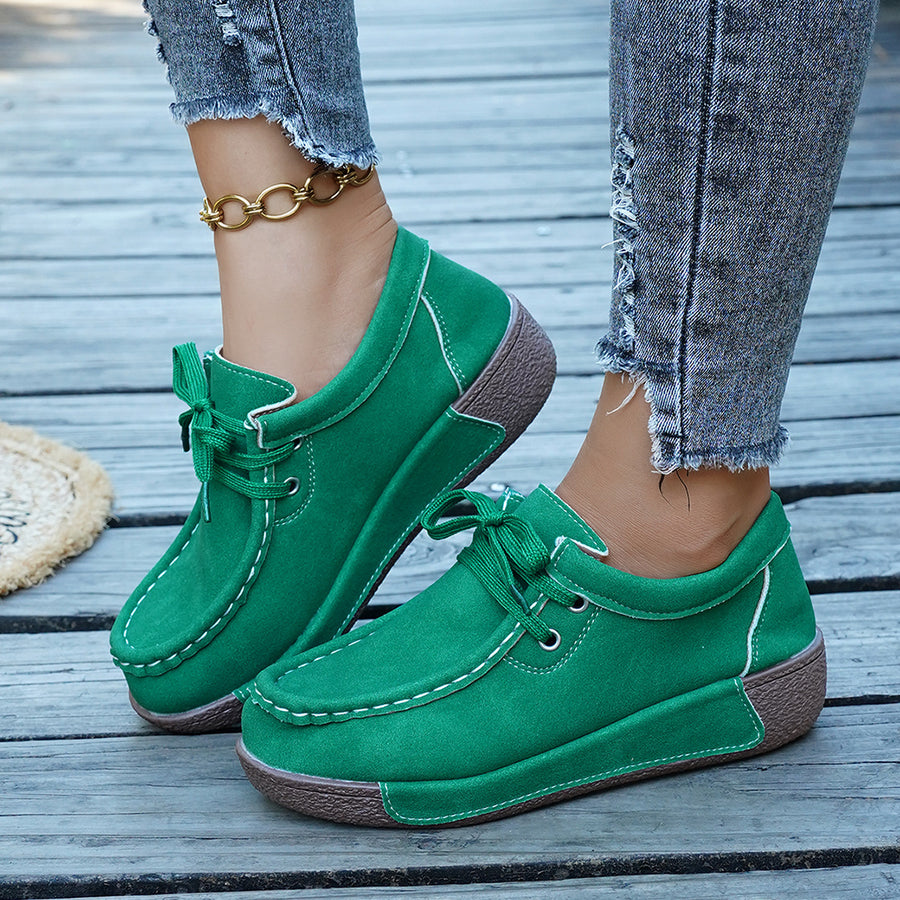 Green lace-up moccasin style sneakers with white stitching and a brown sole.
