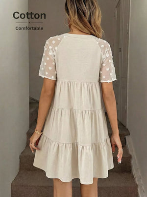 Tiered mini dress in beige cotton with sheer dot sleeves and a ruffled hem.