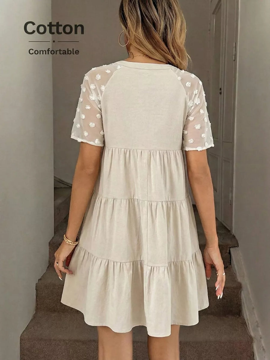 Tiered mini dress in beige cotton with sheer dot sleeves and a ruffled hem.