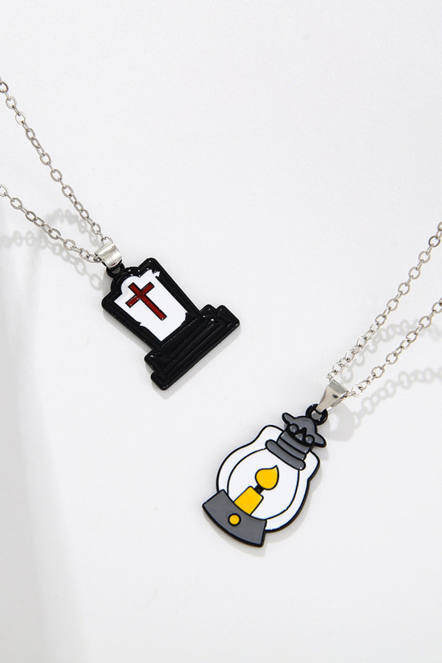 Spooky season enamel pendant necklaces, one tombstone with cross, one lantern with candle.