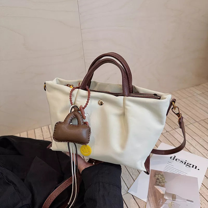 White compact nylon handbag with brown leather accents and charms.