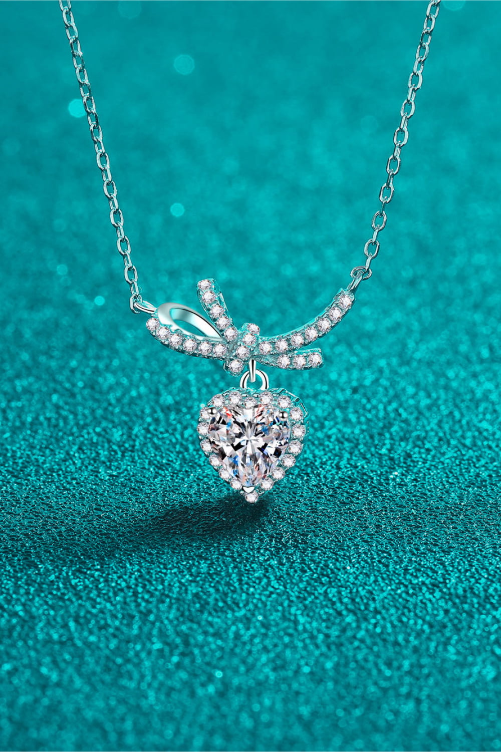 Silver necklace with heart-shaped cubic zirconia pendant and bow accent.