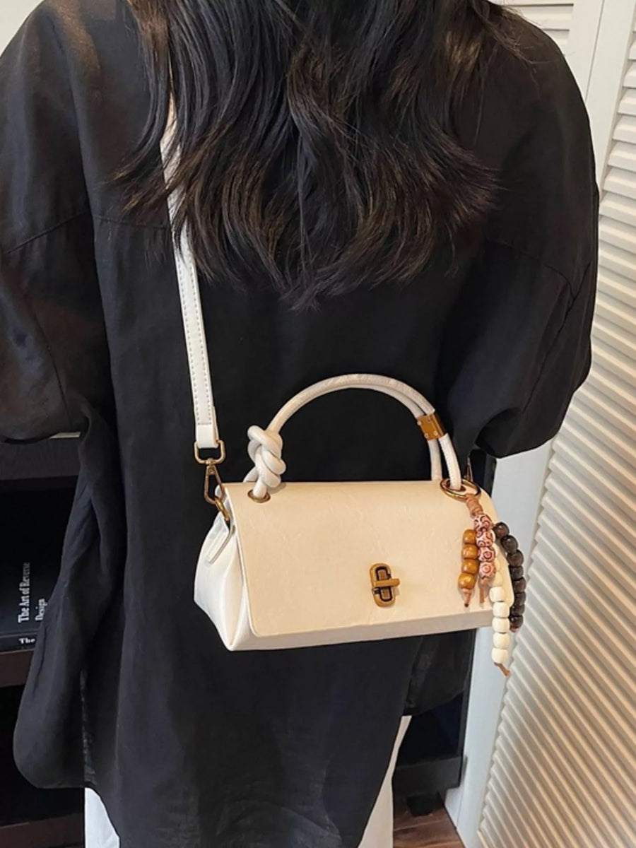 Ivory leather crossbody bag with knotted handle and beaded charm detail.
