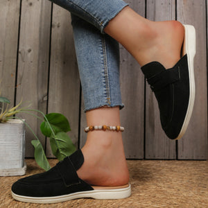 Black backless loafers with textured round toe and strap detail.