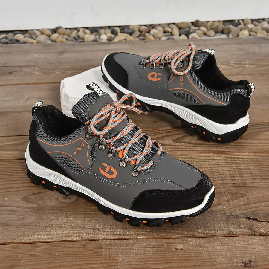 Grey low-top sneakers with patterned orange and grey laces and orange accents.
