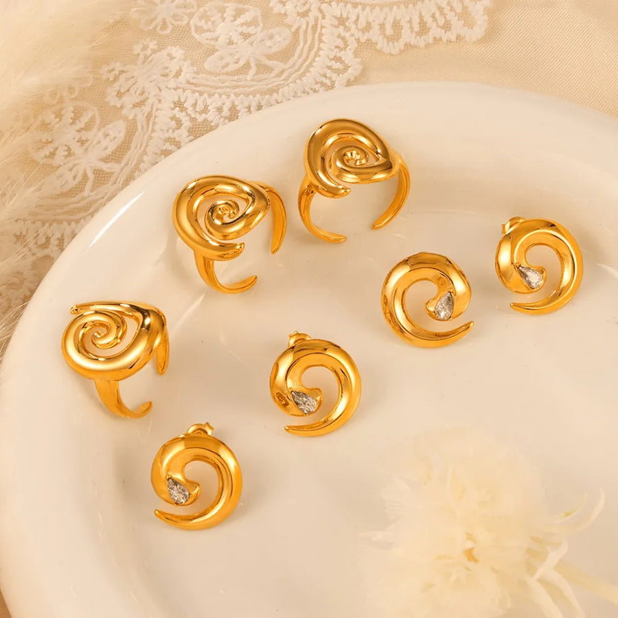 Gold swirl stud earrings with zirconia accents and matching rings.