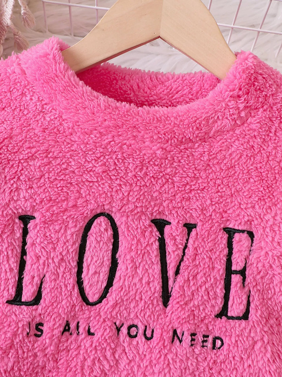 Fuzzy hot pink sweatshirt for kids with black embroidered LOVE and IS ALL YOU NEED text.